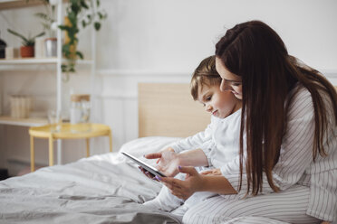 Mother and baby boy using tablet computer while sitting on bed - CAVF44530