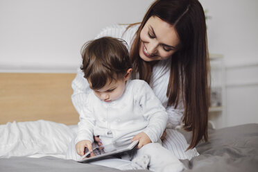 Glückliche Mutter, die einen Tablet-Computer mit einem kleinen Jungen benutzt, während sie auf dem Bett sitzt - CAVF44531