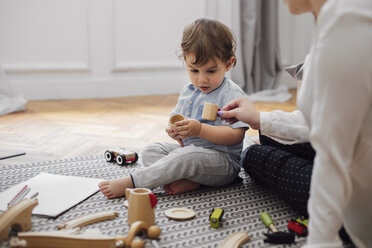 Midsection of mother giving toy teacup to baby boy while sitting on rug at home - CAVF44532