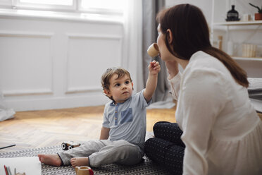 Baby boy looking at mother drinking from toy teacup at home - CAVF44533