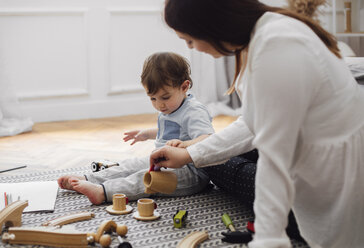 Ein kleiner Junge sieht seine Mutter an, wie sie Tee in eine Spielzeugteetasse gießt - CAVF44534