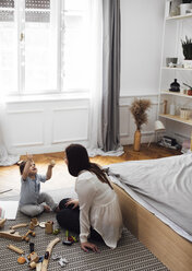 High angle view of baby boy holding toy teacup while sitting with mother on rug in bedroom - CAVF44536