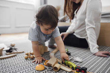 Baby boy playing with miniature train by mother on rug at home - CAVF44537