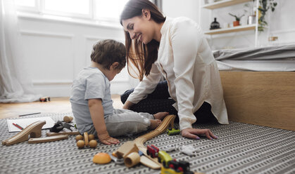 Happy mother and baby boy playing with toys on rug at home - CAVF44538