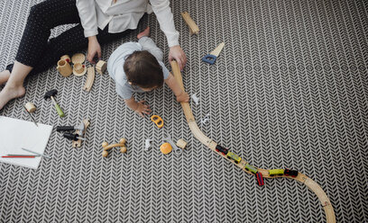 High angle view of mother and baby boy playing with miniature train on rug at home - CAVF44540