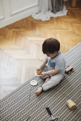 High angle view of baby boy playing with toy teacup and saucer on rug at home - CAVF44542