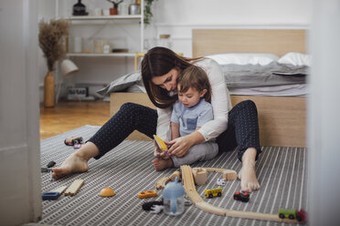 Mother and son playing with toys on rug in bedroom - CAVF44543