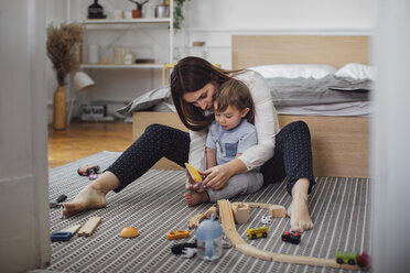 Mutter und Sohn spielen mit Spielzeug auf dem Teppich im Schlafzimmer - CAVF44543