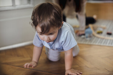 Cute baby boy crawling on Harwood floor with mother in background - CAVF44544