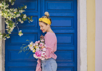 Seitenansicht einer Frau, die wegschaut und einen Blumenstrauß gegen die Tür hält - CAVF44557