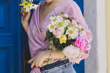 Mittelteil einer Frau, die einen Blumenstrauß hält und gegen eine Tür steht - CAVF44559