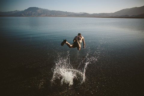 High angle view of shirtless man jumping into lake against mountains stock photo