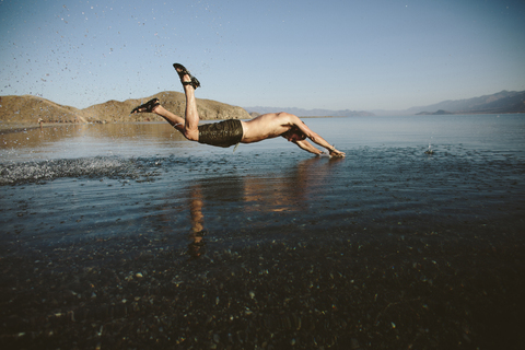 Seitenansicht eines in den See springenden Mannes ohne Hemd gegen den klaren Himmel, lizenzfreies Stockfoto