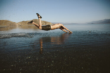 Side view of shirtless man jumping into lake against clear sky - CAVF44570