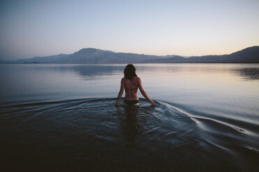 Rückansicht einer Frau, die einen Bikini trägt, während sie in der Abenddämmerung in einem See gegen den klaren Himmel steht - CAVF44575