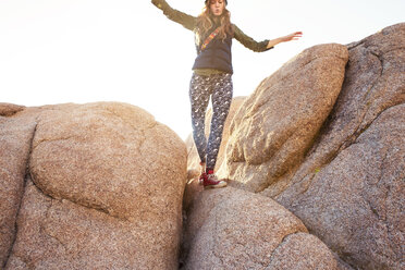 Low angle view of playful woman with arms outstretched walking on rock against sky - CAVF44590