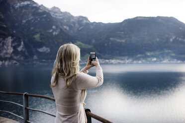 Rückansicht einer Frau, die Meer und Berge fotografiert - CAVF44613