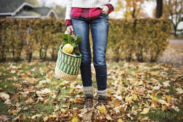 Low section of woman holding shopping bag and standing on messy field - CAVF44630