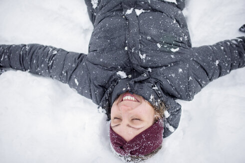 Glückliche Frau mit ausgestreckten Armen auf einem schneebedeckten Feld liegend - CAVF44646