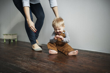 Low section of mother standing by cheerful baby boy sitting on floor at home - CAVF44660