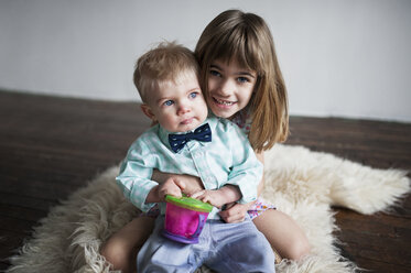 Porträt eines glücklichen Mädchens, das mit einem kleinen Jungen auf einem Teppich zu Hause sitzt - CAVF44668