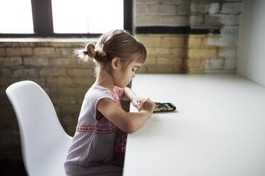 Seitenansicht eines Mädchens, das ein Smartphone am Tisch benutzt - CAVF44673
