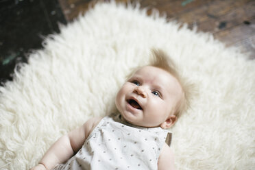 Hohe Winkel Ansicht von Baby-Mädchen schaut weg, während auf pelzigen Teppich zu Hause liegen - CAVF44678