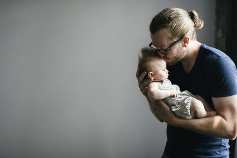 Vater küsst schlafende Tochter und trägt sie vor grauem Hintergrund, lizenzfreies Stockfoto