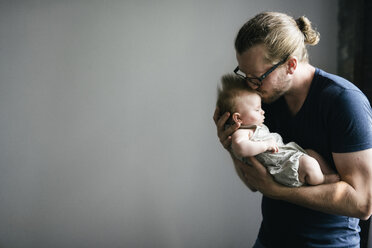 Father kissing sleeping daughter while carrying her against gray background - CAVF44681