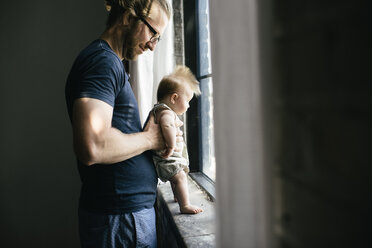 Side view of father and daughter looking through window - CAVF44683