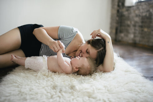 Mother playing with daughter while lying on furry rug at home - CAVF44687