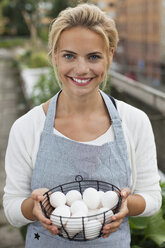 Porträt einer glücklichen jungen Frau in Schürze, die eine Schale mit Eiern hält - MASF06066
