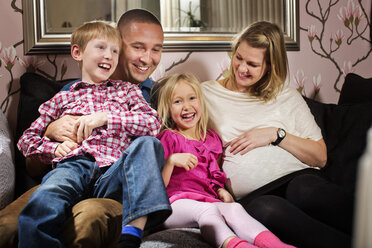 Porträt eines glücklichen Mädchens, das mit seiner Familie auf dem Sofa zu Hause sitzt - MASF06099