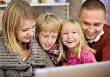 Porträt eines glücklichen Mädchens mit Familie, das zu Hause einen Laptop benutzt - MASF06103