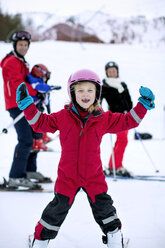Porträt eines glücklichen Mädchens beim Skifahren mit Familie im Hintergrund - MASF06110