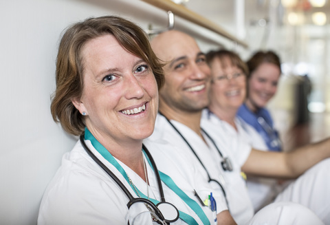 Porträt einer glücklichen reifen Ärztin mit Kollegen, die sich im Krankenhaus an die Wand lehnen, lizenzfreies Stockfoto