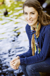 Porträt einer lächelnden Frau, die am See sitzt - CAVF44745