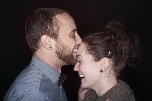 Side view of happy couple standing against black background - CAVF44749