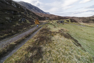 Rear view of woman walking on footpath amidst field and mountains - CAVF44791