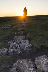 Rückansicht einer Frau auf einem grasbewachsenen Hügel gegen den Himmel bei Sonnenuntergang - CAVF44793