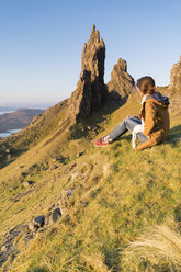 Full length side view of woman sitting hill by rock formations against clear sky - CAVF44795