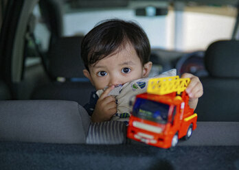 Porträt eines süßen Jungen, der mit einem Spielzeuglastwagen im Auto spielt - CAVF44820