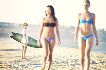 Man looking at women in bikini walking on sand at beach - CAVF44906