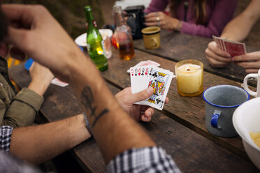 Cropped image of friends playing cards at picnic table in forest - CAVF44974