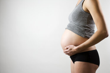 Midsection of a pregnant woman with hand on stomach over gray background - MASF06147