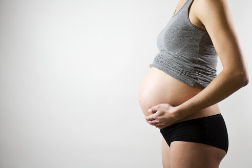 Mittelteil einer schwangeren Frau mit Hand auf dem Bauch auf grauem Hintergrund - MASF06147