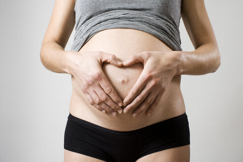Mittelteil einer schwangeren Frau mit Händen, die auf dem Bauch eine Herzform bilden - MASF06148
