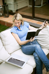 Mittlere erwachsene Frau auf Sofa sitzend mit Buch und Laptop - MASF06151
