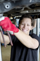 Porträt eines selbstbewussten jungen männlichen Mechanikers, der in einer Werkstatt unter einem Auto arbeitet - MASF06184