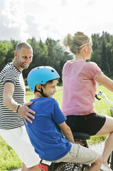 Mann betrachtet seinen Sohn, der hinter einer Frau auf einem Fahrrad im Park sitzt - MASF06223
